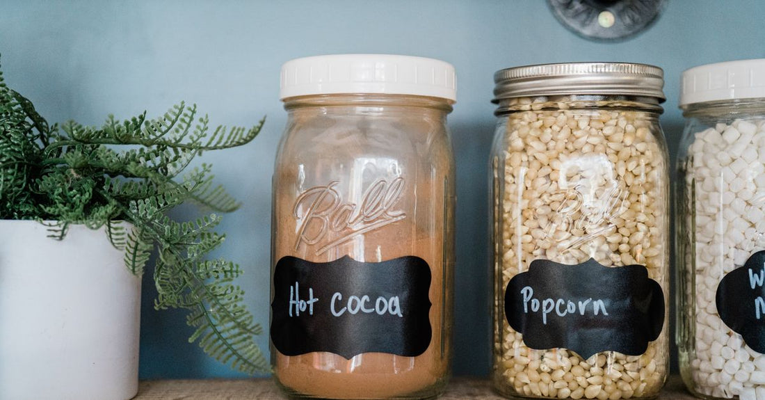 Assorted jars of colourful powdered drink mixes and flavorings on a clean white shelf, illustrating the variety in a powdered drink mixes & flavorings buying guide UK.