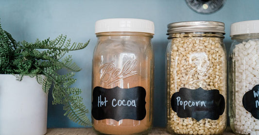 Assorted jars of colourful powdered drink mixes and flavorings on a clean white shelf, illustrating the variety in a powdered drink mixes & flavorings buying guide UK.