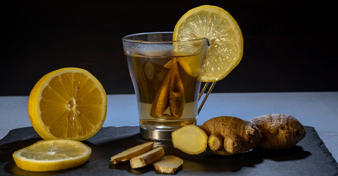 A glass mug of turmeric and ginger tea with fresh turmeric root and ginger slices on a wooden table.