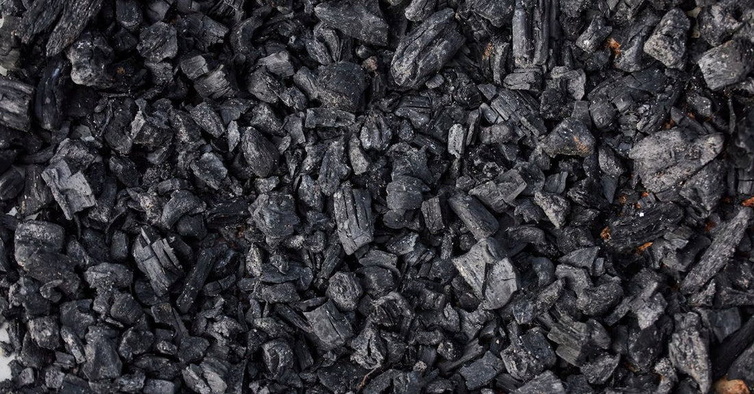 A jar of activated charcoal powder beside a scattering of black capsules on a white surface, representing the best charcoal UK 2026 options.
