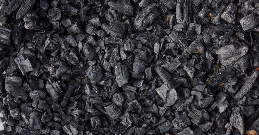 A jar of activated charcoal powder beside a scattering of black capsules on a white surface, representing the best charcoal UK 2026 options.