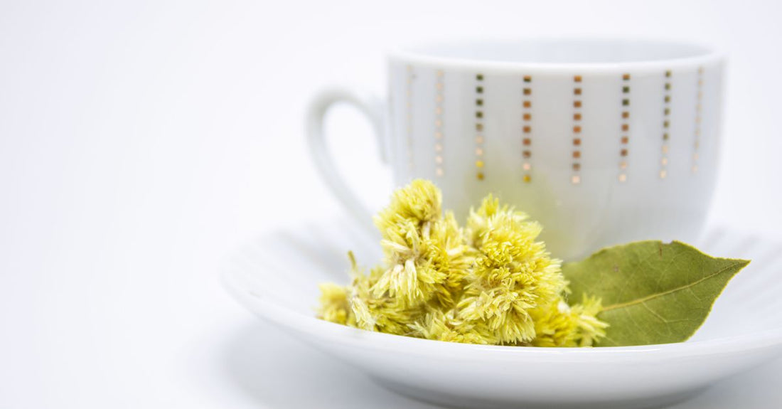 A steaming cup of mullein tea for cough relief, with dried mullein leaves and a strainer on a wooden table.