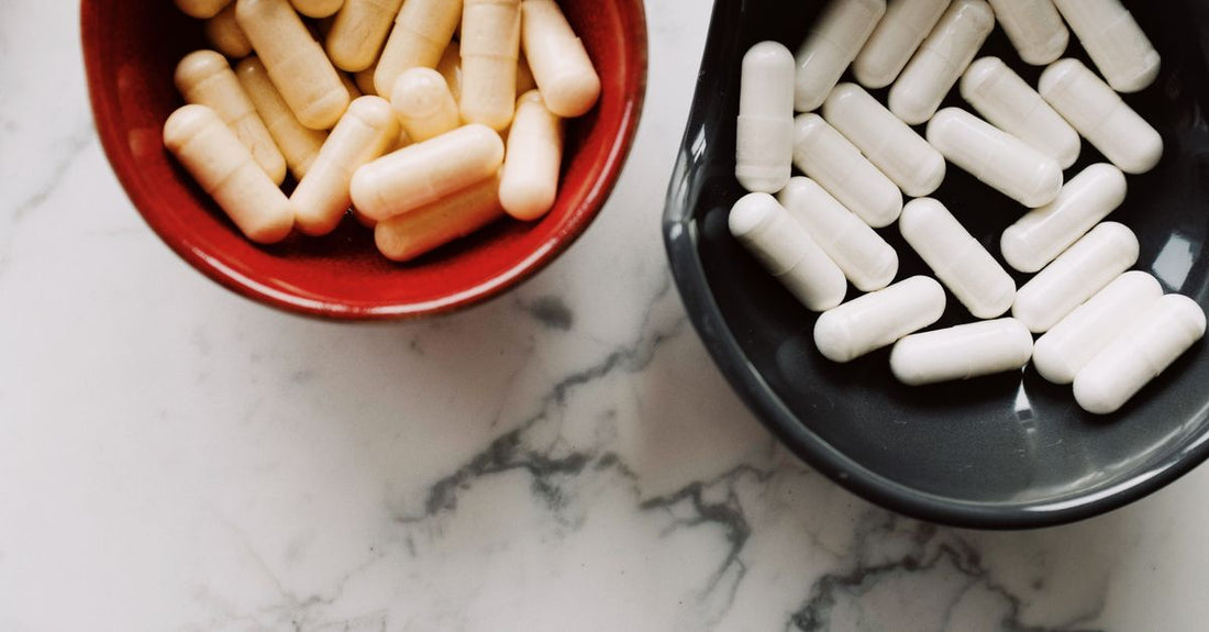 A white bottle of probiotic capsules beside a glass of water on a light wooden surface, illustrating a probiotics buying guide UK for gut health.