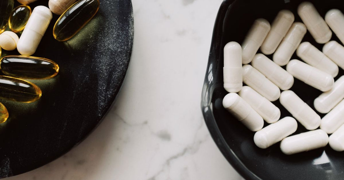 A close-up of ashwagandha capsules with black pepper beside dried ashwagandha root on a neutral background
