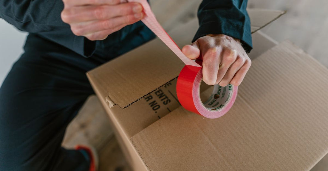 Assorted adhesive tapes and glues on a neutral surface, illustrating how to choose adhesives & tapes for various surfaces.