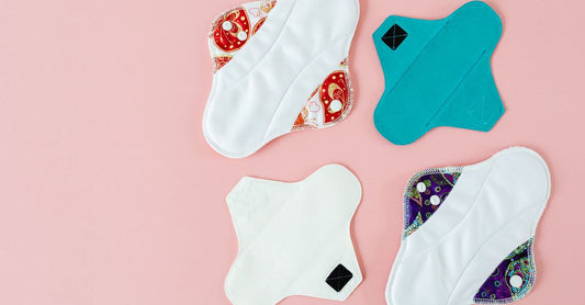 A pack of four blue reusable underpads stacked on a white bed, showing quilted texture and stitched edges.