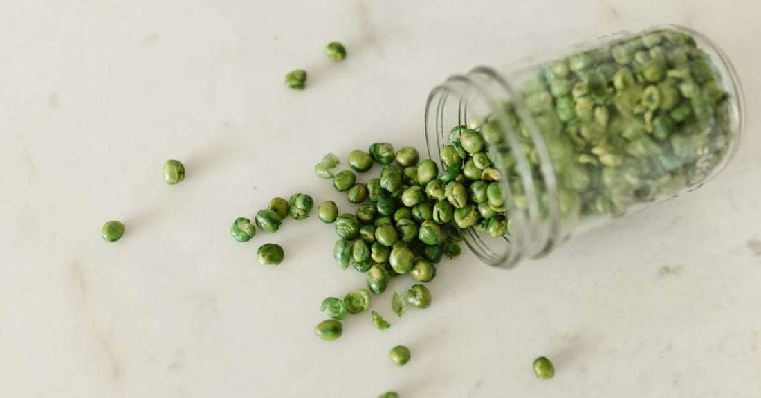 A jar of unflavoured pea protein isolate powder with a scoop on a kitchen counter
