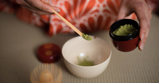 A bowl of vibrant matcha green tea powder with a bamboo whisk on a neutral background, illustrating how to choose green tea UK.